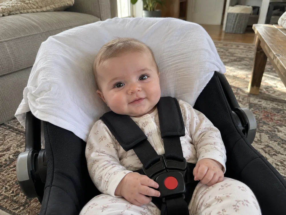 A baby in a car seat with a white sheet draped behind